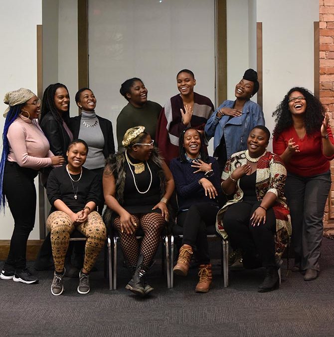 A group of 11 people are in a room looking at the camera, laughing.